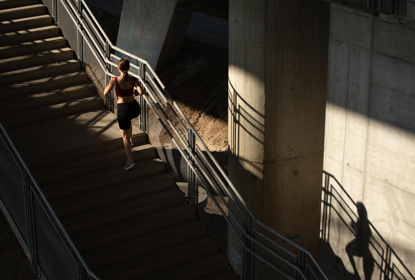 Runner ascending concrete stairs in a modern architectural setting with strong light and shadow