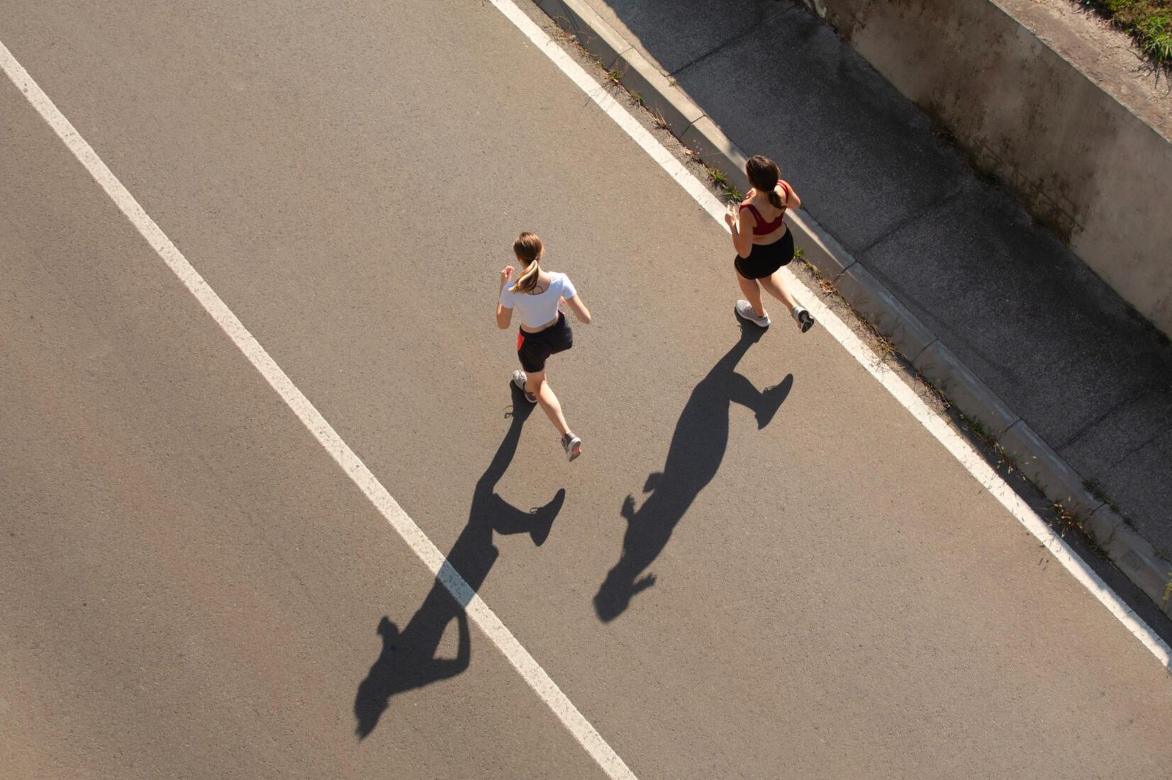 Two runner moving along a divided roadway from an overhead perspective.